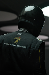 A race car driver in a black racing suit and helmet, standing with their back to the camera, in a dimly lit environment with circular lights overhead. | Lamborghini Store | Official Website